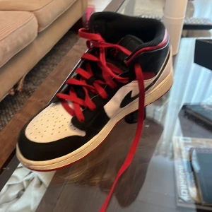 Nike Air Jordans med röd snörning - Snygga Nike Air Jordans i svart, vitt och rött. Skorna har en klassisk design med röd snörning och svart swoosh. Perfekta för dig som vill ha en stilren och sportig look.