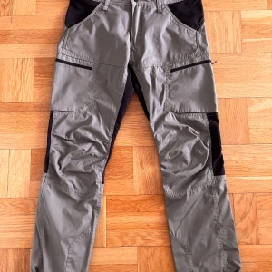  Friluftsbyxor från McKinley - Säljer ett par gröna friluftsbyxor från McKinley i storlek XL. Byxorna har svarta detaljer och flera praktiska fickor med dragkedja. Perfekta för utomhusaktiviteter med slitstarkt material och bekväm passform.