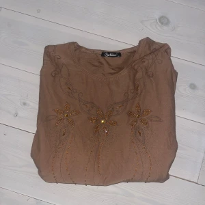 Brun topp med pärlbroderier - Säljer en brun långärmad topp från Öyküm med vackra broderade blommor och pärlor framtill. Säljer pga kommer ej t användning 