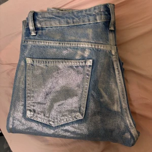 Silverfärgade jeans - Snygga  jeans med en glittrig finish. De har en klassisk femficksdesign och bälteshällor. Perfekta för att sticka ut med en unik stil.