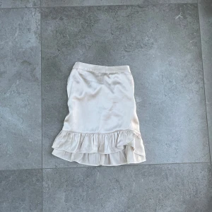  kjol med volang - Säljer en elegant kjol med volangdetalj i nederkant. Kjolen har en mjuk och glansig yta som ger en lyxig känsla. Perfekt för att piffa upp garderoben med något stilrent och klassiskt.