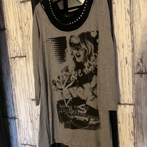 Grå klänning med tryck från KappAhl - Säljer en grå klänning från KappAhl med ett coolt tryck framtill och nitar runt halsringningen. Klänningen har långa ärmar och en avslappnad passform. Perfekt för en avslappnad stil med en touch av rock.