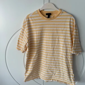 Gul och vit randig t-shirt från H&M - Säljer en gul och vit randig t-shirt från H&M med relaxed fit. Perfekt för en avslappnad stil. T-shirten är kortärmad och gjord i mjukt material för extra komfort.