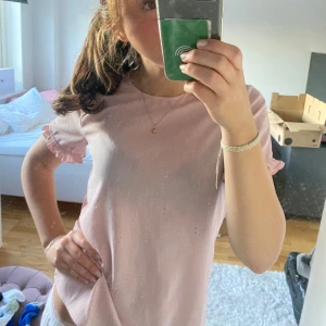 Rosa topp - Säljer en söt rosa topp med korta ärmar och volangdetaljer vid ärmsluten. Perfekt för en avslappnad och stilren look. Toppen är i en mjuk och bekväm kvalitet.
