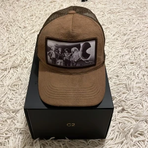 Brun keps från Maggiore - Snygg brun keps från Maggiore med ett coolt tryck på framsidan. Kepsen har en klassisk design med nät baktill för extra ventilation. Perfekt för en avslappnad stil. 