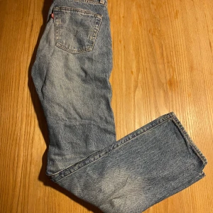 Levis 501 jeans - Klassiska Levis 501 jeans i blå denim. De har en rak passform och är tillverkade i slitstarkt jeanstyg. Byxorna har en knappgylf och fem fickor, med den ikoniska Levis-lappen på baksidan. Defekt ser ni på sista bilden där det är en liten skråma och lite missfärgat