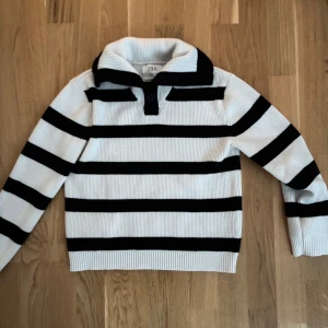 Randig stickad tröja med krage - Säljer en snygg randig tröja från Zara barn i svart och vit, med krage som man viker ner. Tröjan har gulliga knappar framtill och passar mig som har strl XS