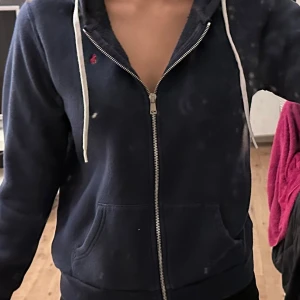 Ralph lauren mörkblå hoodie  - Säljer en mörkblå hoodie med dragkedja och vit snörning. Köpt för 2300 kr.