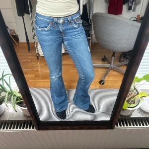 Blå jeans från True Religion - Snygga blå jeans från True Religion med bootcut-stil och låg midja. De har klassiska fem fickor och märkets ikoniska broderi på bakfickorna. 