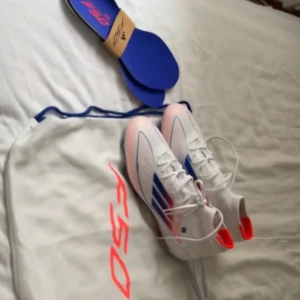 Adidas fotbollsskor med blå och röda detaljer - Snygga fotbollsskor från Adidas med blå och röda detaljer. Skorna har en vit bas med snörning och en slitstark sula med dobbar för bra grepp på planen. Perfekta för fotbollsträning och matcher. Dem är använda ungefär 3 gånger, är helt som nya skor. Anledningen till att jag säljer dem är att dem inte passar mig. OBS!! Endast seriösa köpare. Priset kan diskuteras!!