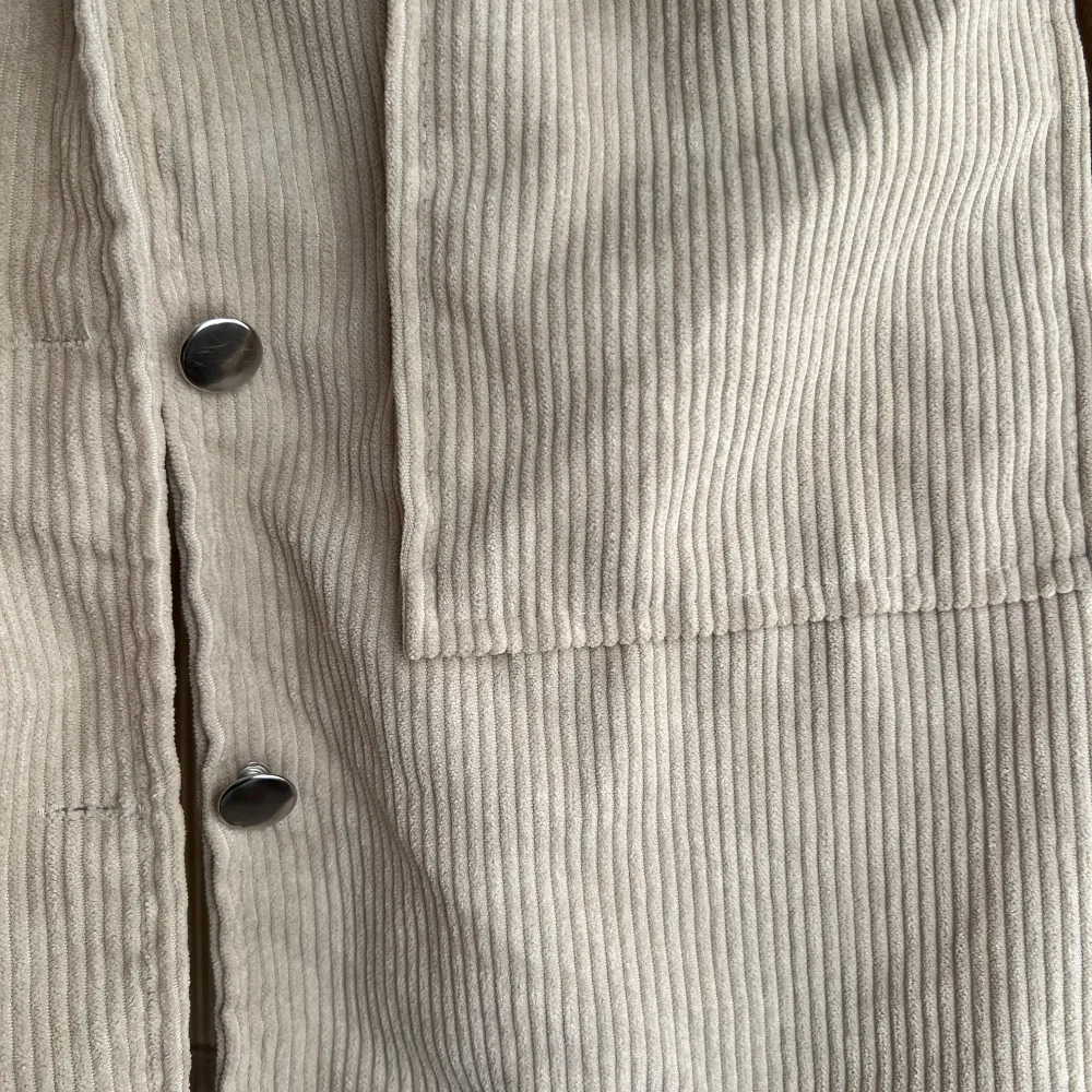 Säljer en snygg beige manchesterjacka med knappar framtill. Jackan har en klassisk krage och två stora fickor på bröstet. Perfekt för en stilren look!. Takit.