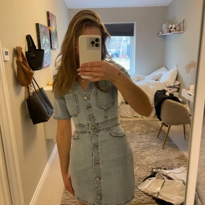 Jeansklänning med knappar - Trendig jeansklänning i ljus denim med korta ärmar och knappar framtill. Klänningen har en v-ringad design och markerad midja för en snygg passform. 