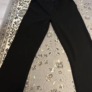 Svarta kostymbyxor från 157 - Snygga svarta kostymbyxor från 157 i storlek M. Byxorna har en klassisk design med knappstängning och bälteshällor. Perfekta för en stilren look. Blivit för stora på mig. Byxan är stor i storlek så passar L bättre. 