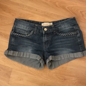 Blå jeansshorts  - Snygga blå jeansshorts med flätade detaljer på fickorna. De har en klassisk femficksdesign och uppvikta benslut. Perfekta för en avslappnad stil.