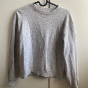 Grå sweatshirt  - Säljer en stilren grå sweatshirt i ekologisk bomull. Tröjan har en klassisk design med rund hals och långa ärmar. Perfekt för en avslappnad look. Använd fåtal gånger. 