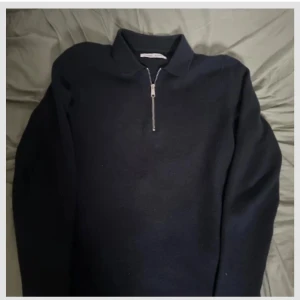 Navy blå tröja med dragkedja från Samsoe Samsoe - Säljer en stilren svart tröja från Samsoe Samsoe  med dragkedja framtill. Tröjan har långa ärmar och en klassisk krage, perfekt för en minimalistisk look. Passar bra till både jeans och chinos.