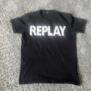 Svart t-shirt från Replay - Säljer en svart t-shirt från Replay med stort vitt tryck på framsidan. T-shirten har en rund halsringning och korta ärmar. Perfekt för en avslappnad stil.