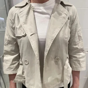 Beige trenchcoat med knappar - En beige trenchcoat med knappar och trekvartsärmar. Perfekt för vår och höst! 💕💕