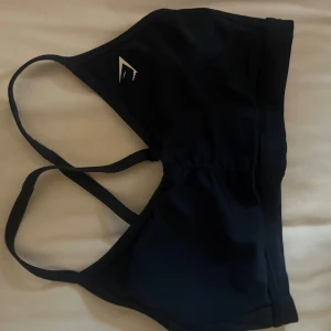 Mörkblå sport-bh från Gymshark - Säljer en mörkblå sport-bh från Gymshark med justerbara axelband och en liten logga på framsidan. Perfekt för träning och ger bra stöd. Materialet är mjukt och stretchigt för bästa komfort.
