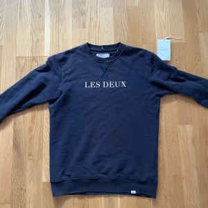Sweatshirt från Les Deux - Säljer en stilren svart sweatshirt från Les Deux med deras logga tryckt på bröstet. Tröjan har långa ärmar och en klassisk rund halsringning. Skriv gärna vid funderingar!