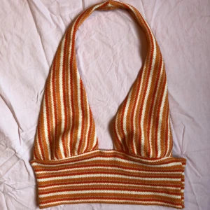 Randig stickad halterneck topp -  snygg randig halterneck topp i orange och vit. Toppen är stickad och har en croppad passform som är perfekt för sommaren. Den har ett retroinspirerat mönster med breda ränder som sitter ihop i nacken 