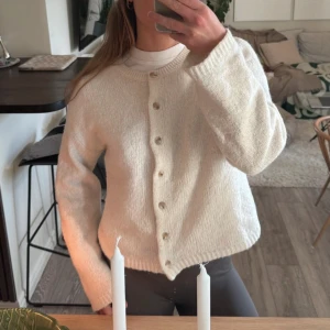 Vit stickad kofta - Mysig vit stickad kofta med knappar framtill. Perfekt för kyliga dagar och ger en stilren look. Långärmad design som passar bra över en t-shirt eller blus.