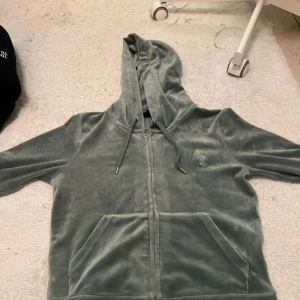 Grön velour hoodie från Juicy Couture - Säljer en snygg grön velour hoodie från Juicy Couture. Den har dragkedja framtill och en bekväm huva med snörning. Perfekt för en avslappnad stil. Matchande byxor finns också tillgängliga. En av dem för 300/400 kr eller båda för 700