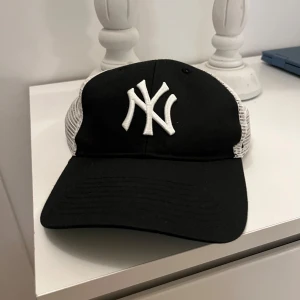 New York Yankees keps - Snygg svart keps med vit broderad logga framtill och vita nätpaneler på sidorna och baksidan. Justerbar passform med plastspänne. Perfekt för en avslappnad stil.