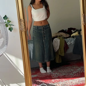 Mörkblå jeanskjol med knappar - Säljer en mörkblå lång jeanskjol med snygga kontrastsömmar och flera knappar framtill. Kjolen har fickor både fram och bak samt bälteshällor i midjan. Modellen är A-linjeformad och ger en retro vibe. Den passar S eller M beroende på ifall man vill ha den hög eller lågmidjad! Märket är vintage vero Moda😋