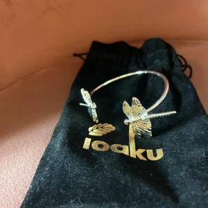 Silverfärgat armband med trollsländor från Ioaku - Unikt armband i silverfärg från Ioaku med två detaljerade trollsländor i ändarna. Snygg och stilren design som verkligen sticker ut. Kommer med svart tygpåse med guldfärgad logga. Perfekt accessoar för dig som gillar naturinspirerade smycken. Säljer det då det inte kommer till användning, köpt för 599kr