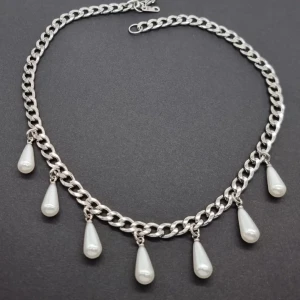 Silver halsband med droppformade pärlor - Stilrent halsband i silverfärgad kedja med sju hängande droppformade vita pärlor. Kedjan har chunky länkar som ger en cool vibe och pärlorna ger en elegant touch. Perfekt för att lyfta din outfit med lite extra bling och unik stil.