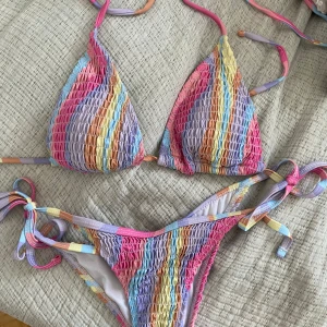 Färgglad bikini med snörning - Säljer en superfin bikini med färgglada ränder i lila, rosa, blå, gul och orange. Bikinin har trekantsformad överdel och knytband både upptill och på sidorna av underdelen. 