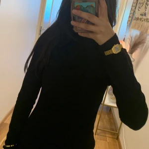 tunn Svart ribbad tröja - Svart polotröja med ribbad struktur och lång ärm. Tröjan har en tight passform och är gjord i mjukt material som sitter skönt mot kroppen. Perfekt för lager-på-lager och funkar till både jeans och kjol. Enkel och stilren design utan detaljer.