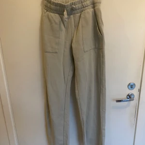 Grågrön mjukisbyxor med snörning - Snygga grågrön mjukisbyxor med hög midja och bred resår samt snörning i midjan. Byxorna har raka ben, stora fickor fram och bak, och är gjorda i mjukt bomullsmaterial. Perfekta för chill dagar eller när du vill vara extra bekväm.