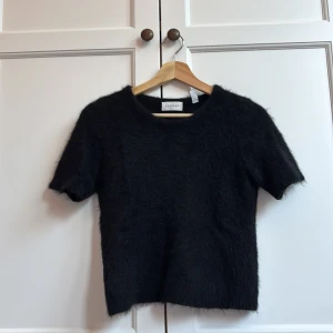 Svart fluffig stickad tröja Dagmar - Säljer en svart stickad tröja från Dagmar med korta ärmar och rund hals. Tröjan har en fluffig och mjuk yta som ger en cool och mysig vibe. Perfekt för dig som gillar stilrena och enkla plagg med lite extra känsla.