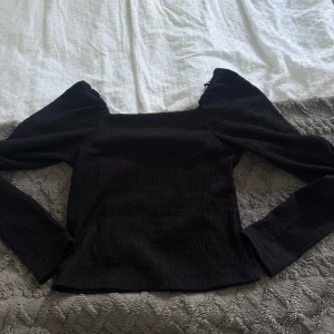 Svart långärmad topp från H&M - Säljer en svart långärmad topp från H&M i storlek XS. Toppen har puffiga axlar och en fyrkantig halsringning som ger en trendig vibe. Materialet är lätt ribbat och stretchigt, vilket gör den bekväm och snygg. Perfekt att styla med jeans eller kjol.