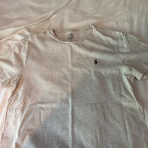 Ljusgrå t-shirt Polo Ralph Lauren - Snygg ljusgrå t-shirt från Polo Ralph Lauren med klassisk rund hals och liten broderad logga på bröstet. Modellen är custom slim fit och har korta ärmar. Perfekt för dig som gillar stilrena och enkla plagg med premiumkänsla. Skicket är som ni ser och fin tshirt.