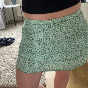 Grön blommig kjol med shorts från Zara - Supersöt grön kortkjol från Zara med vita små blommor och inbyggda shorts under. Kjolen har en volangig design och sitter bekvämt i midjan. Perfekt för dig som vill ha både stil och rörelsefrihet. Passar dig som gillar blommigt och fräscha färger! Jätte fin året runt både till en sommarkväll men också till ett par strumpbyxor och ett par boots 