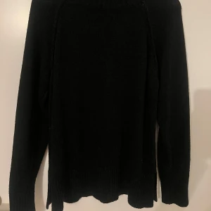 Svart stickad tröja från NA-KD - Svart  stickad polotröja från NA-KD i storlek S. Tröjan har en hög, ribbad krage och långa ärmar och är en längre tröja. Den är stickad och har en loose passform med slitsar i sidorna för extra chill vibe. Perfekt att matcha med jeans eller kjol för en enkel och snygg look. 
