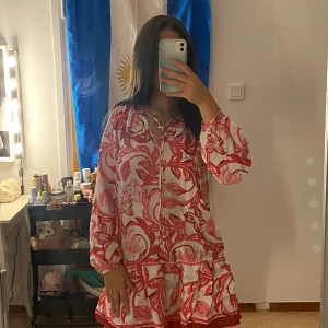 Blommig kortklänning från H&M XS - Säljer en luftig och söt kortklänning från H&M i storlek XS. Klänningen är vit med ett rosa blommigt mönster, har långa ärmar med resår vid handlederna och en v-ringad hals med knyt. Perfekt för sommarens alla tillfällen!