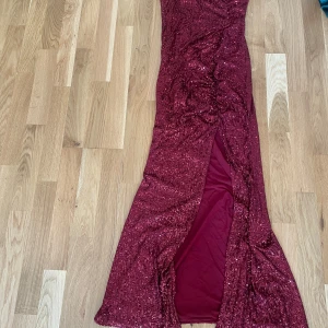 Vinröd glittrig långklänning Fashion Nova - Säljer en vinröd långklänning från Fashion Nova med tunna axelband och glittriga paljetter över hela klänningen. Klänningen har en snygg slits framtill och är figurnära med omlottdetaljer. Materialet är polyester och spandex, vilket gör den stretchig och bekväm.