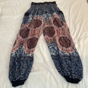 Mönstrade linnebyxor/yogabyxor - Säljer ett par sjukt sköna boho-inspirerade linnebyxor/yogabyxor med elastisk midja och muddar vid bensluten. Byxorna har ett färgstarkt mönster i blått, rött och vitt med mandala- och blommiga detaljer. Perfekta för chill dagar eller yoga.