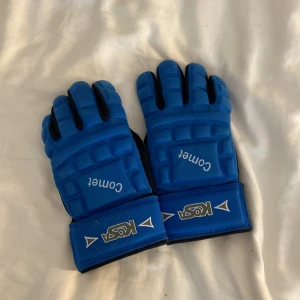 Blå och svarta crosshandskar  - Säljer ett par blå och svarta crosshandskar från Kosa med vadderade paneler och justerbara kardborreband vid handleden. Handskarna har ett coolt, sportigt utseende och är perfekta för dig som gillar att vara aktiv. 