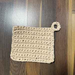  Virkad bej grytlapp  - Ingen bok syns på bilden, endast en beige virkad grytlapp eller underlägg. Ingen information om titel, författare eller innehåll kan utläsas.