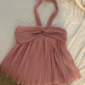 Plisserad rosa halterneck topp - Supersöt plisserad halterneck topp i ljusrosa med twistad detalj framtill. Luftig och flowy modell med breda band som knyts i nacken. Från Zara, Slutsåld.