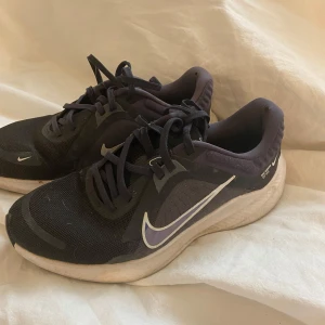 Svarta Nike träningssneakers - Säljer ett par svarta Nike sneakers med vit swoosh och detaljer. Skorna har mesh-ovandel för bra ventilation, snörning och en tjock, vit och svart sula med mönstrad undersida. Perfekta för träning och löpning, riktigt sköna och snygga på foten.