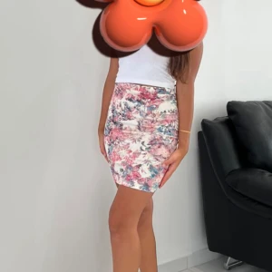 Blommig kortkjol från Warehouse - Supersnygg kortkjol från Warehouse med blommigt mönster i rosa, blått och vitt. Kjolen har en tight passform och är gjord i mjuk polyester som sitter skönt mot kroppen. Perfekt för dig som vill ha en fräsch och färgglad look.