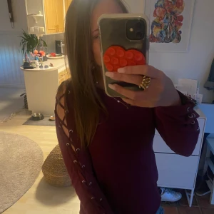 Vinröd långärmad tröja med snörning - Snygg vinröd långärmad tröja med cool snörningsdetalj längs hela ärmen. Tröjan har en slim passform och är perfekt för dig som gillar unika detaljer. Materialet känns mjukt och stretchigt, vilket gör den skön att bära. Passar till jeans eller kjol för en trendig look. Passar både i storlek xs och S