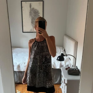 Svart och beige mönstrad kortklänning - Snygg mönstrad klänning i loose passform. Passar både som fest- och strandklänning.