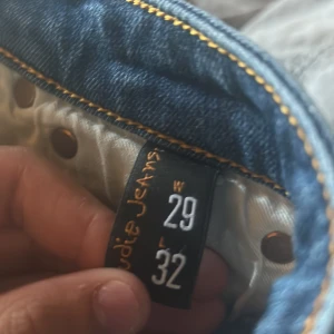 Blå jeans från Nudie Jeans W29 L32 - Snygga blå jeans från Nudie Jeans med klassisk femficksdesign och kontrastsömmar. Jeansen har raka ben och coola broderade detaljer på bakfickorna. Tillverkade i slitstarkt denim med en normal passform som sitter skönt hela dagen.